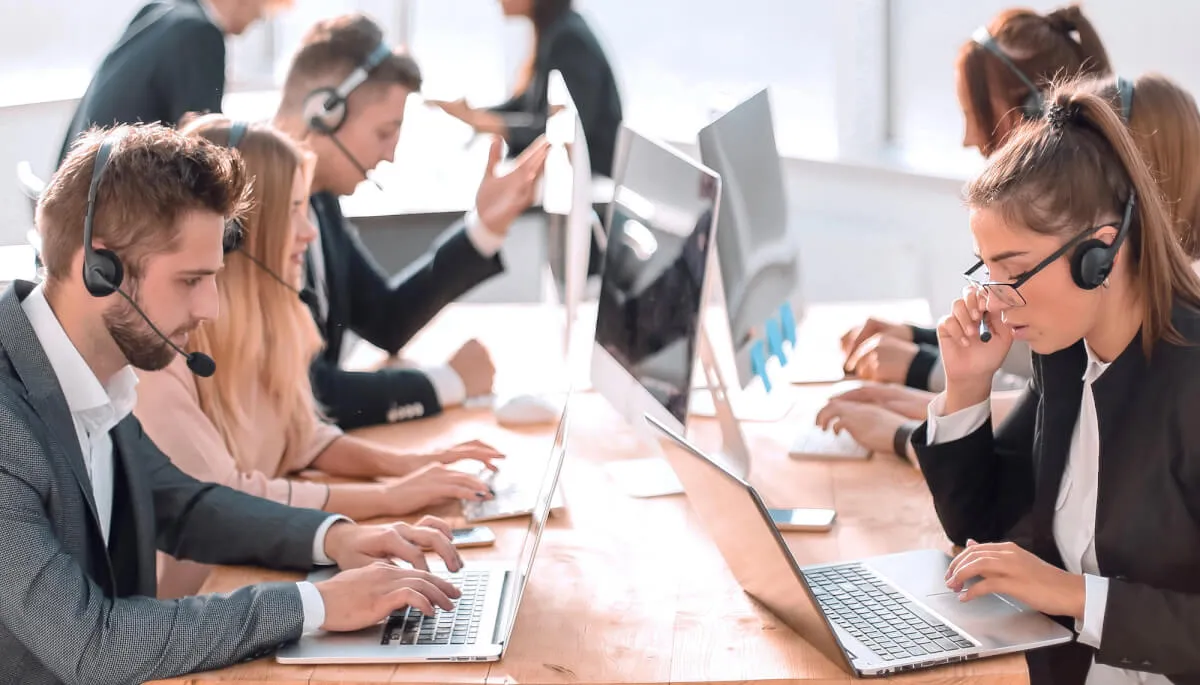 Operatori di un contact center con cuffie e computer portatili seduti a una lunga scrivania